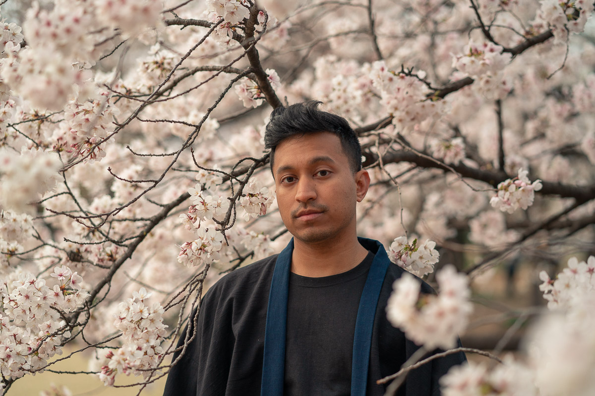 indian guy standing in next to cherry blossoms in japan 
